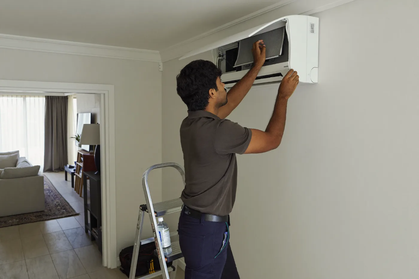 Technician on a step ladder removing the filter from a split AC unit for cleaning