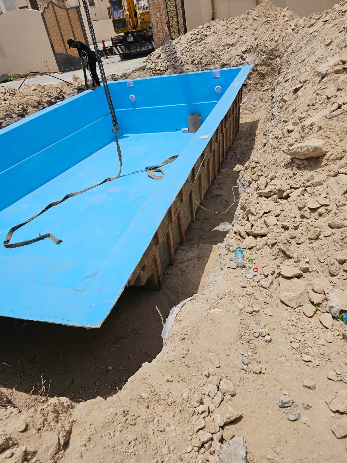 Fiberglass pool shell being lowered into the excavation by crane