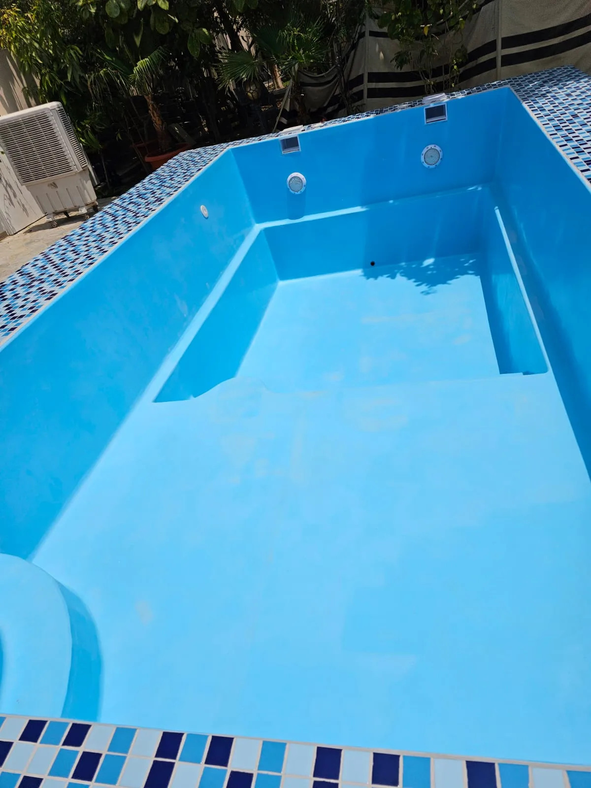 Completed fiberglass pool with blue mosaic tile coping