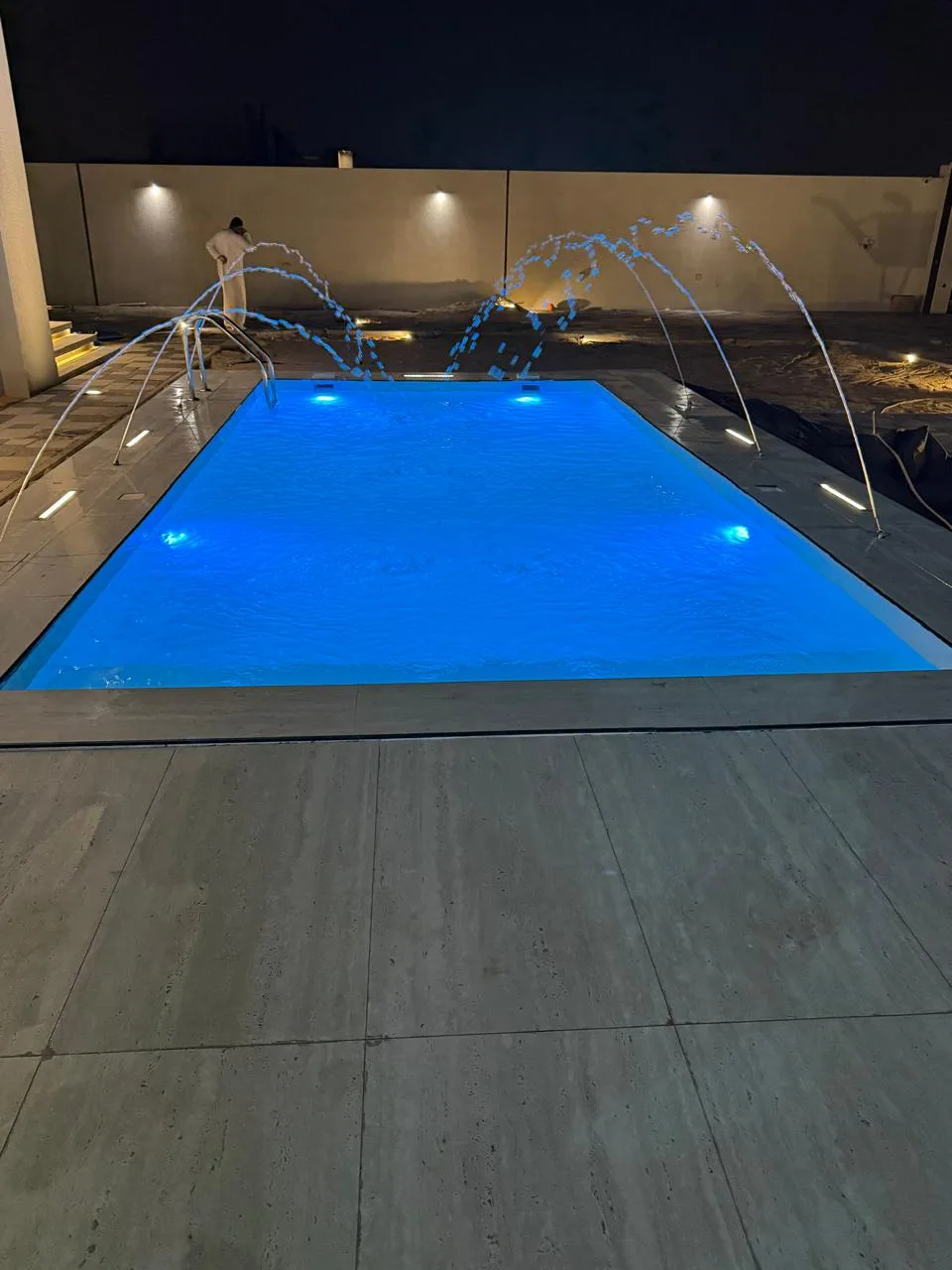 Pool water features arcing over a lit swimming pool at night
