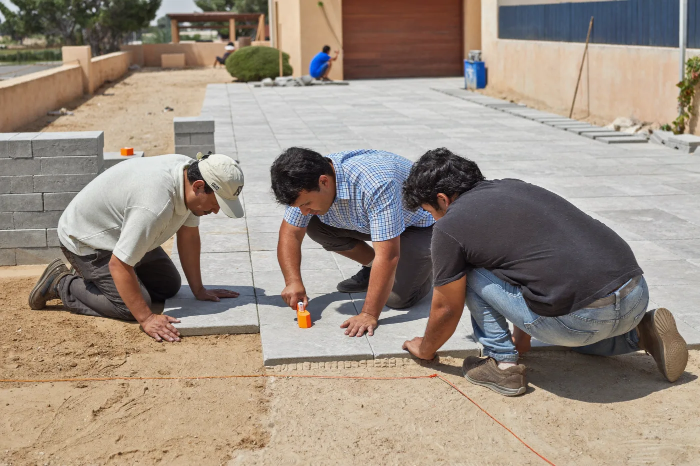 Workers laying interlock paving blocks to a string line on a sand bed