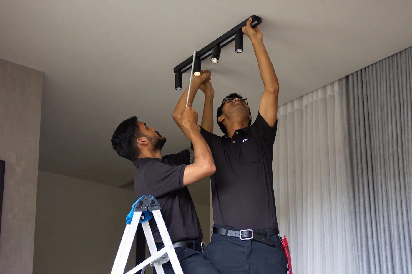 Two technicians working together to adjust a ceiling light fitting